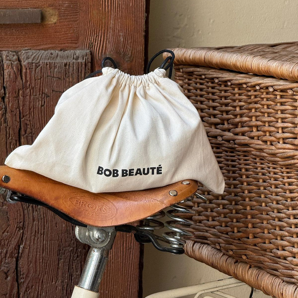 Drawstring bag with 'BOB BEAUTE' branding on a bicycle seat against a rustic background
